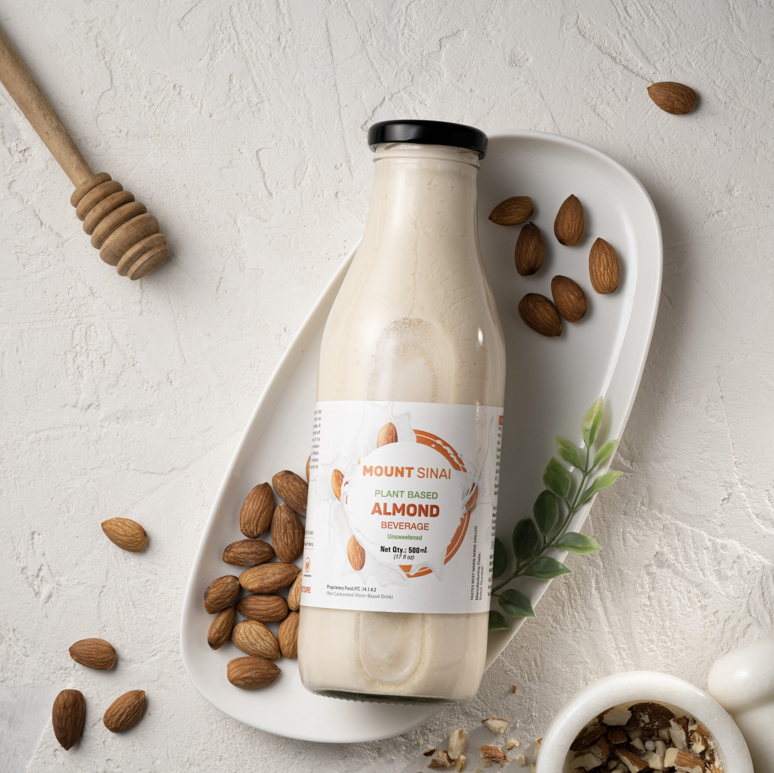 Mount Sinai almond milk bottle on a ceramic tray, surrounded by almonds, honey dipper, and nuts.